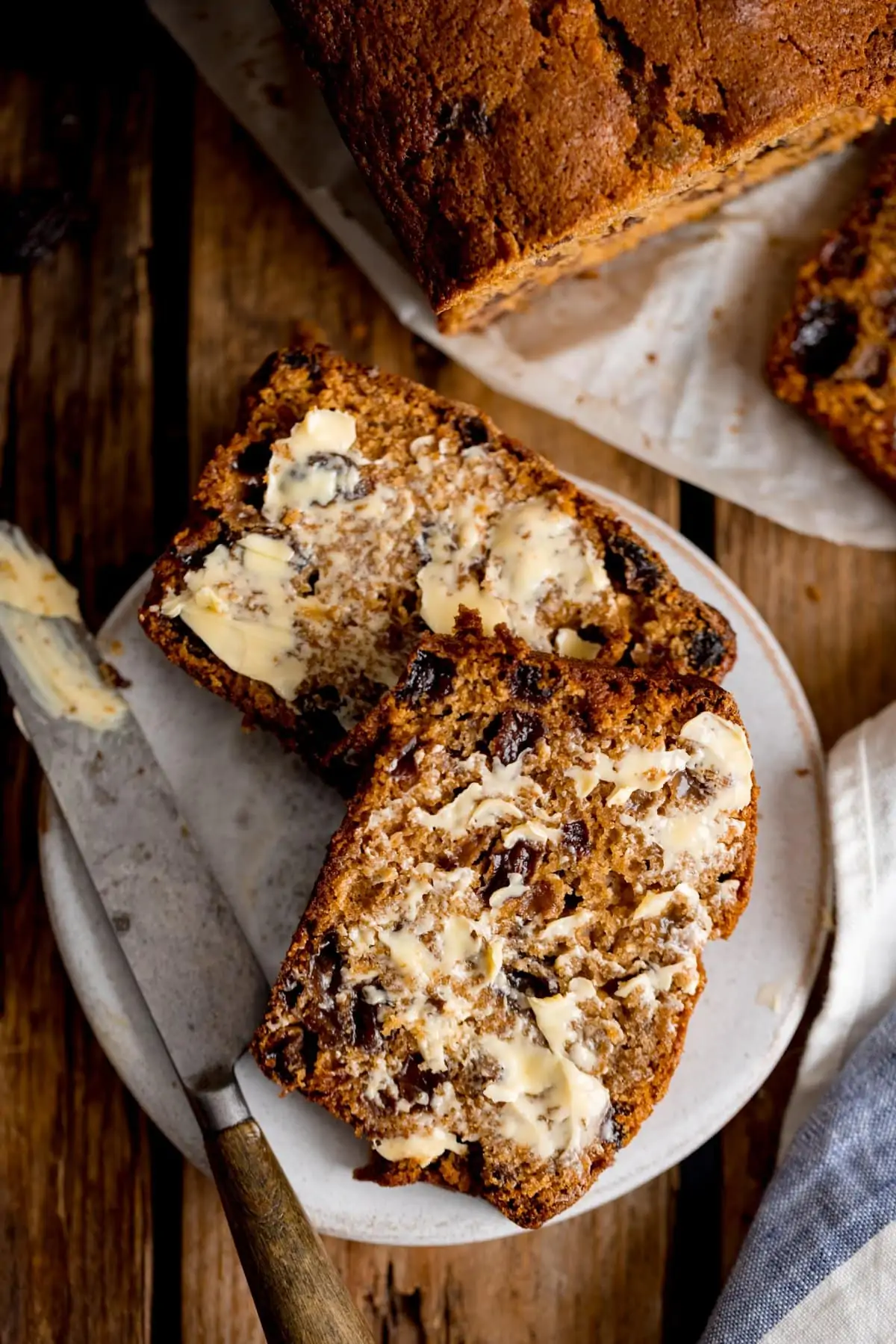 Slices of buttered tea loaf on a plate with a butter knife. Rest of the cake in the background.