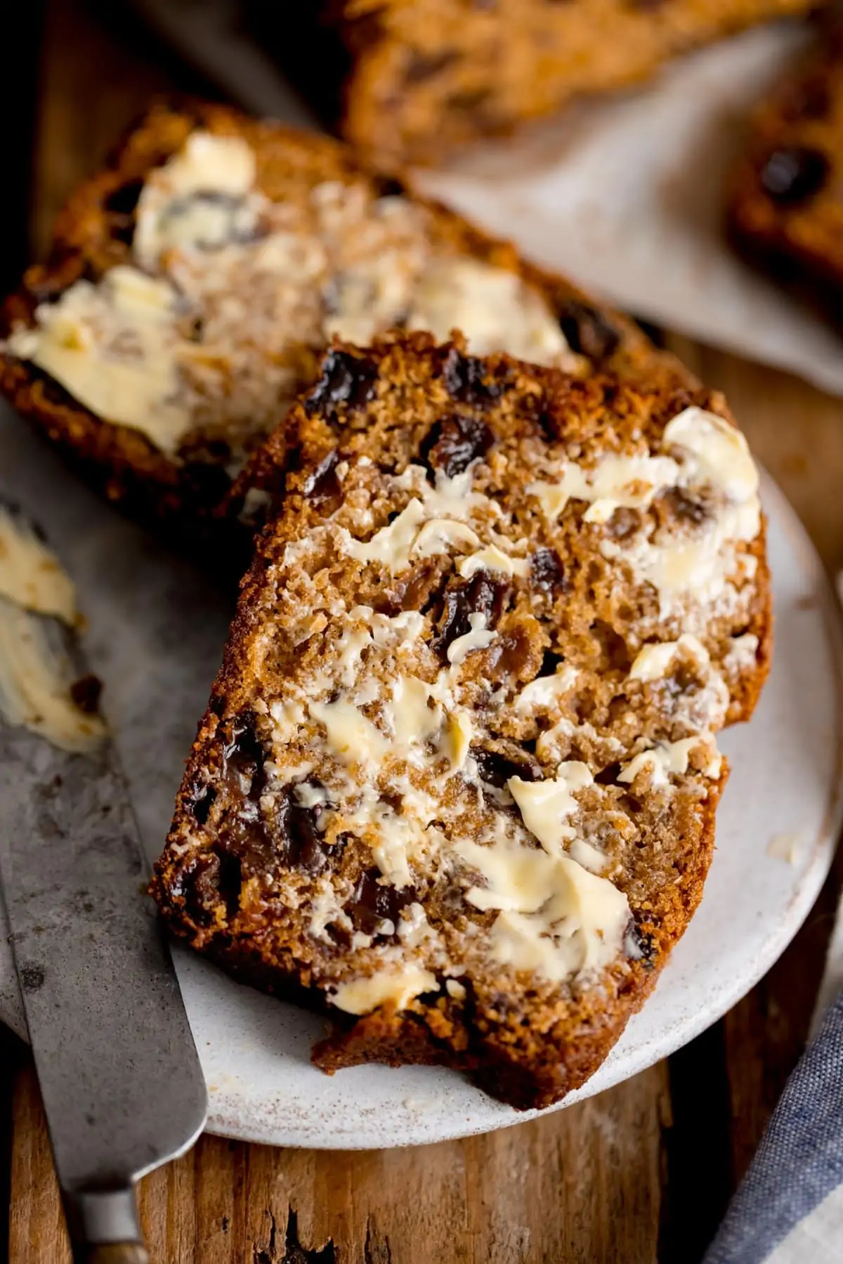 Two slices of buttered tea loaf on a white plate. Knife also in shot.