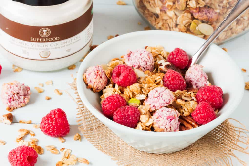 coconut granola in a bowl with raspberries and coconut oil in the background