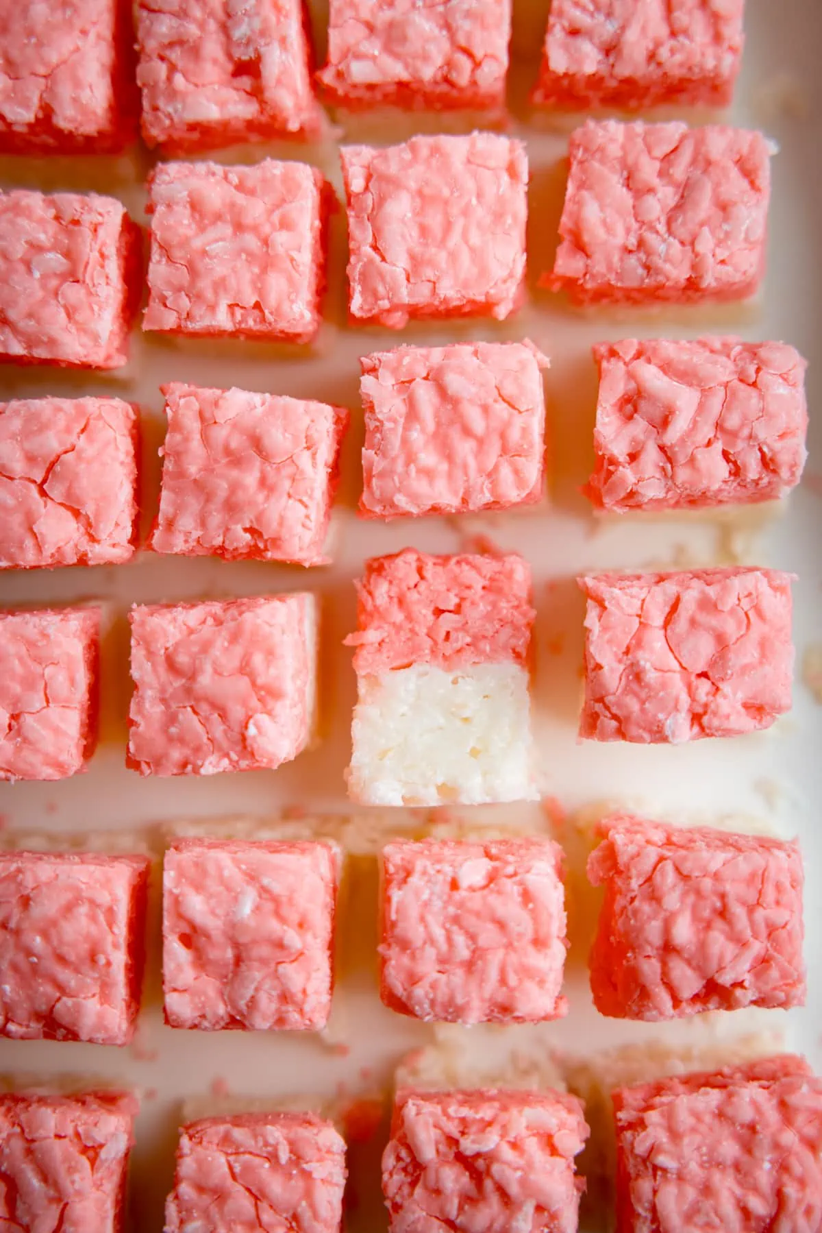 Close up overhead image of pink and white coconut ice squares on a white board. One of the coconut ice squares is on its side.