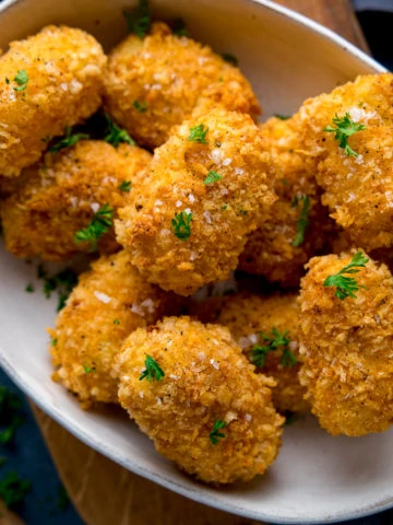 Close up image of potato croquettes in a white bowl sprinkled with parsely