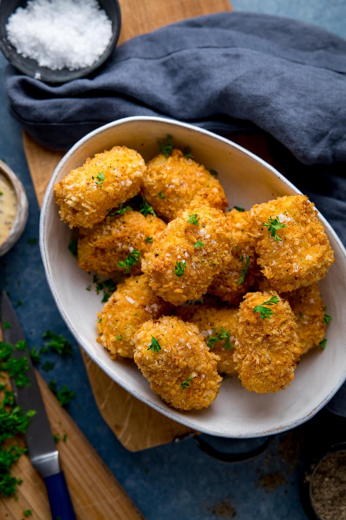 potato croquettes in a white bowl on a wooden board next to a blue napkin