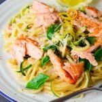 White plate topped with spaghetti, zoodles, sugarsnap peas, flaked salmon and lemon zest