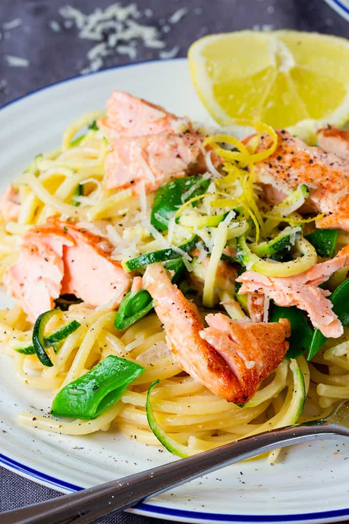 White plate topped with spaghetti, zoodles, sugarsnap peas, flaked salmon and lemon zest