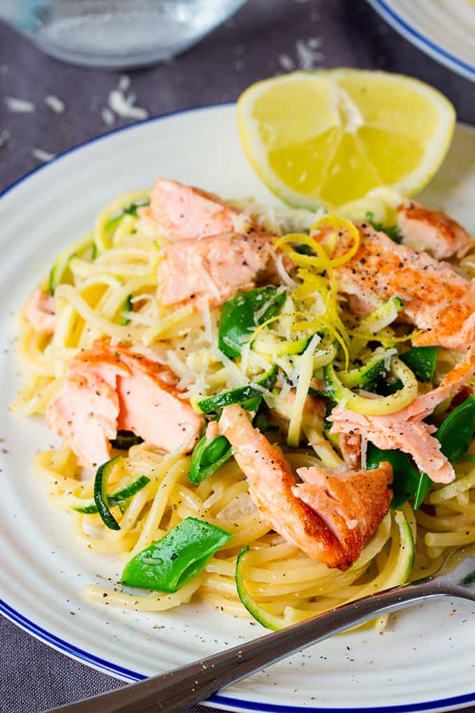 White plate topped with spaghetti, zoodles, sugarsnap peas, flaked salmon, lemon zest and a lemon wedge