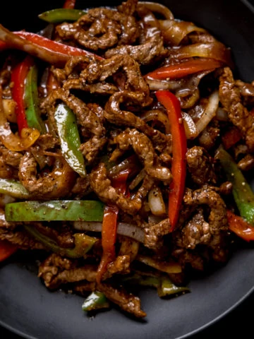 Black pepper beef stir fry with red and green peppers in a black bowl