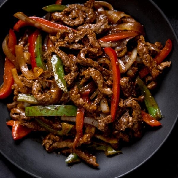 Black pepper beef stir fry with red and green peppers in a black bowl