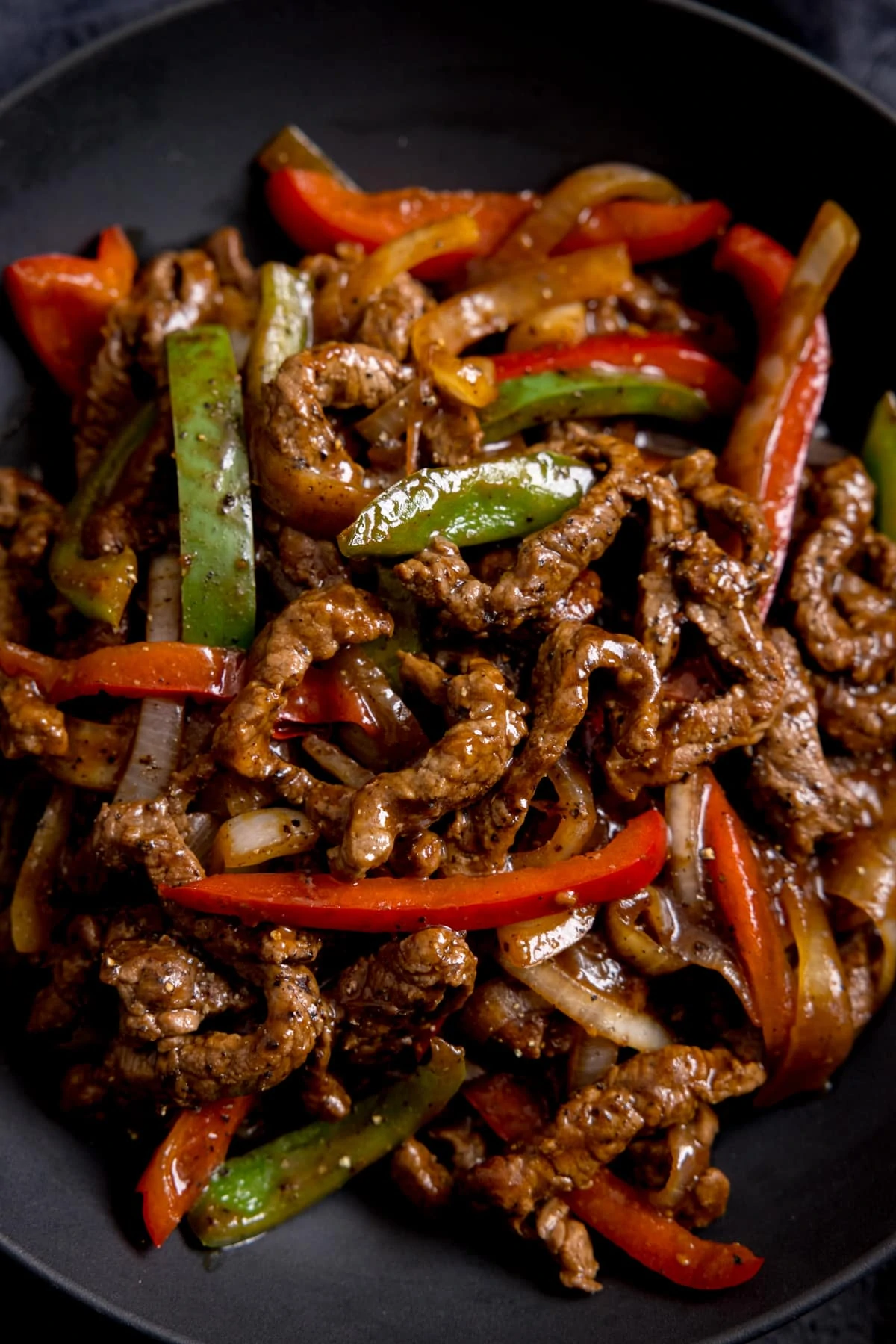Close up of black pepper beef stir fry with red and green peppers in a bowl