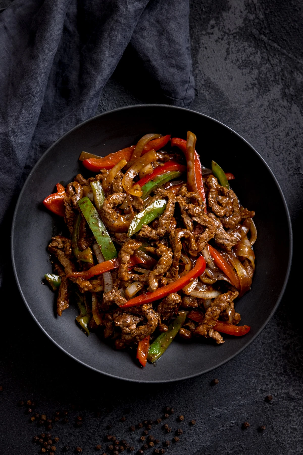 Black pepper beef stir fry in a black bowl on a dark background.