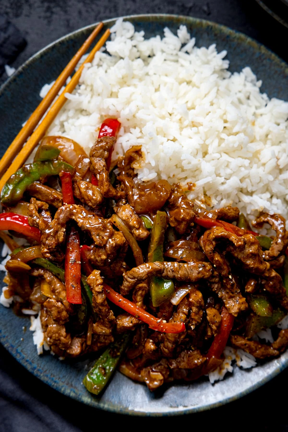 Black pepper beef stir fry with red and green peppers in a black bowl with boiled rice.