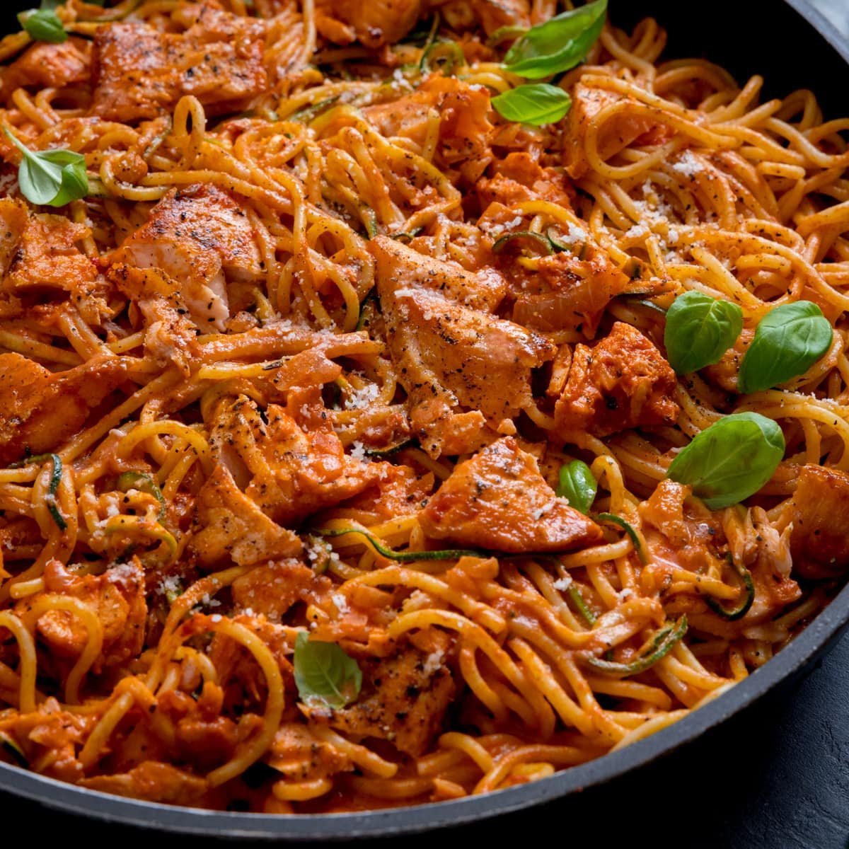 Spaghetti and pieces of salmon on a creamy tomato sauce in a pan