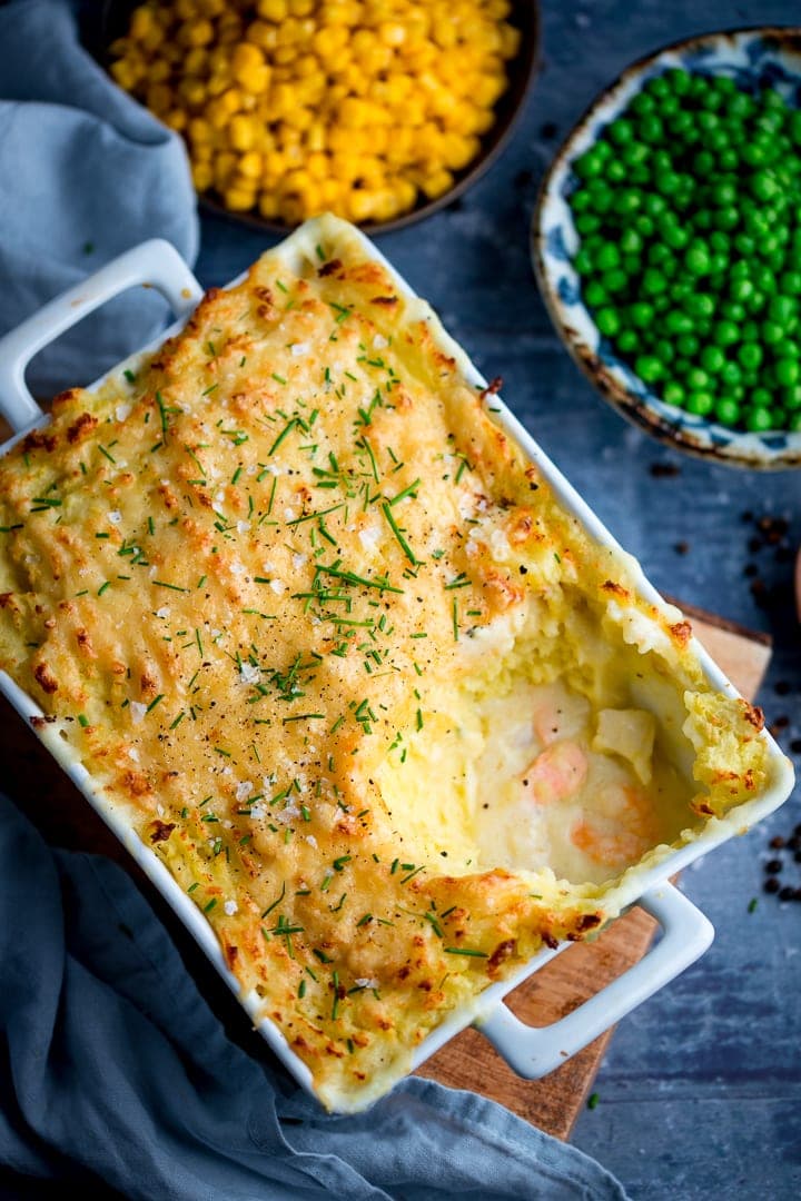Fish pie with mashed potato on a blue background. Peas and corn in background.