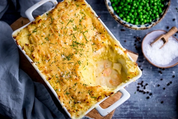 mixed seafood topped with mashed potatoes in a rectangular dish on a wooden board