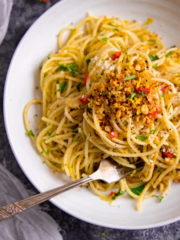 Spaghetti with garlic breadcrumbs and red chilli on a white plate.