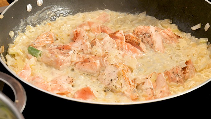 Flakes of salmon fillet poaching in a pan in a cream sauce with onions