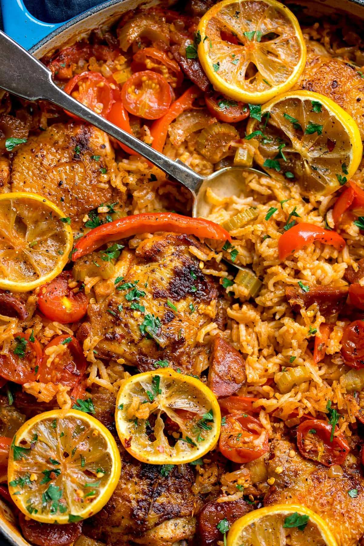 Overhead of Spanish chicken and rice with lemon slices, tomato and red peppers in a blue pan