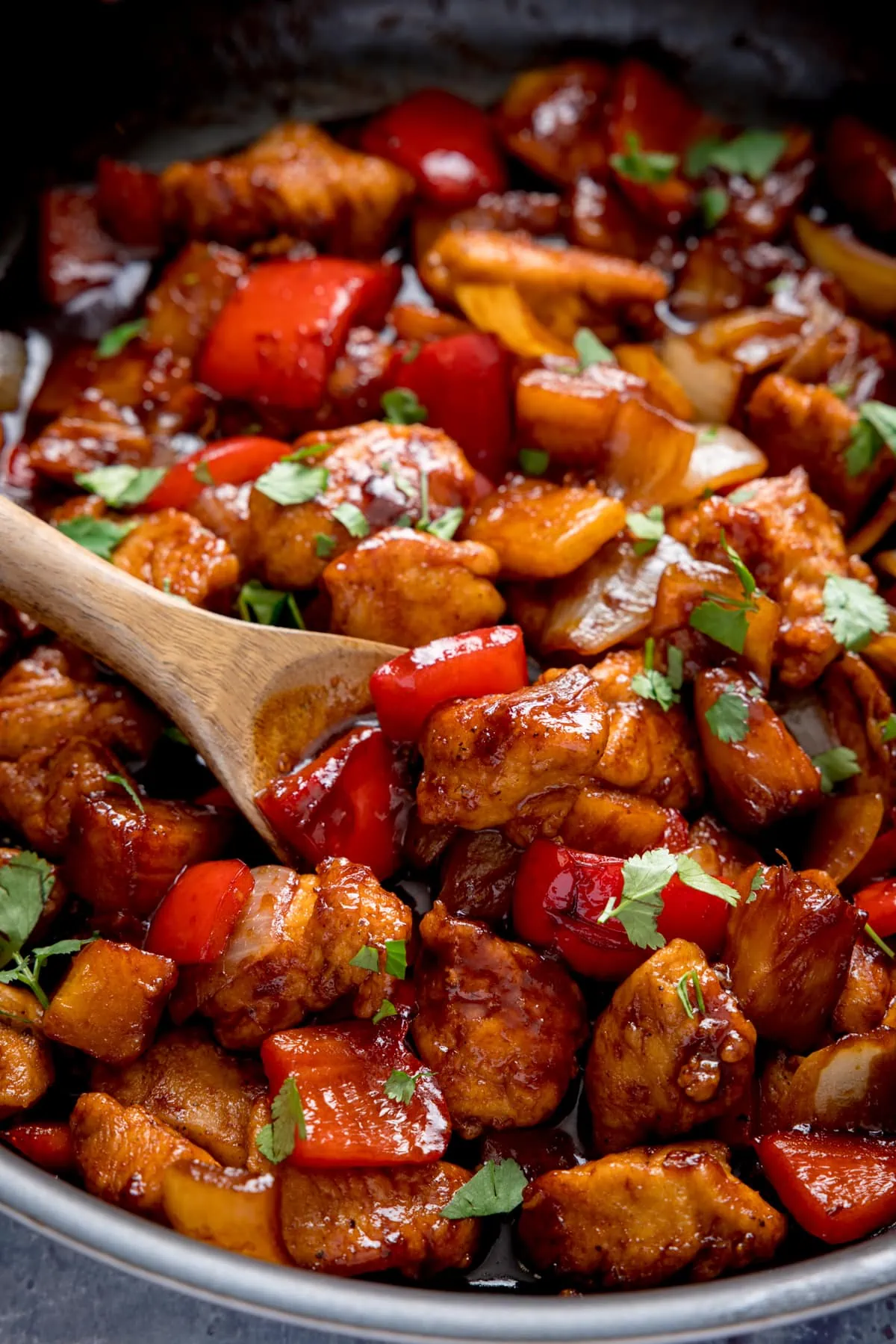 Close up of Sticky Pineapple Chicken Stir Fry in a pan, with a wooden spoon being used to stir the chicken.