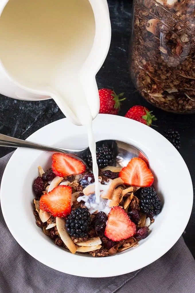 Pouring milk onto a bowl of chocolate coconut granola with cranberries with strawberries