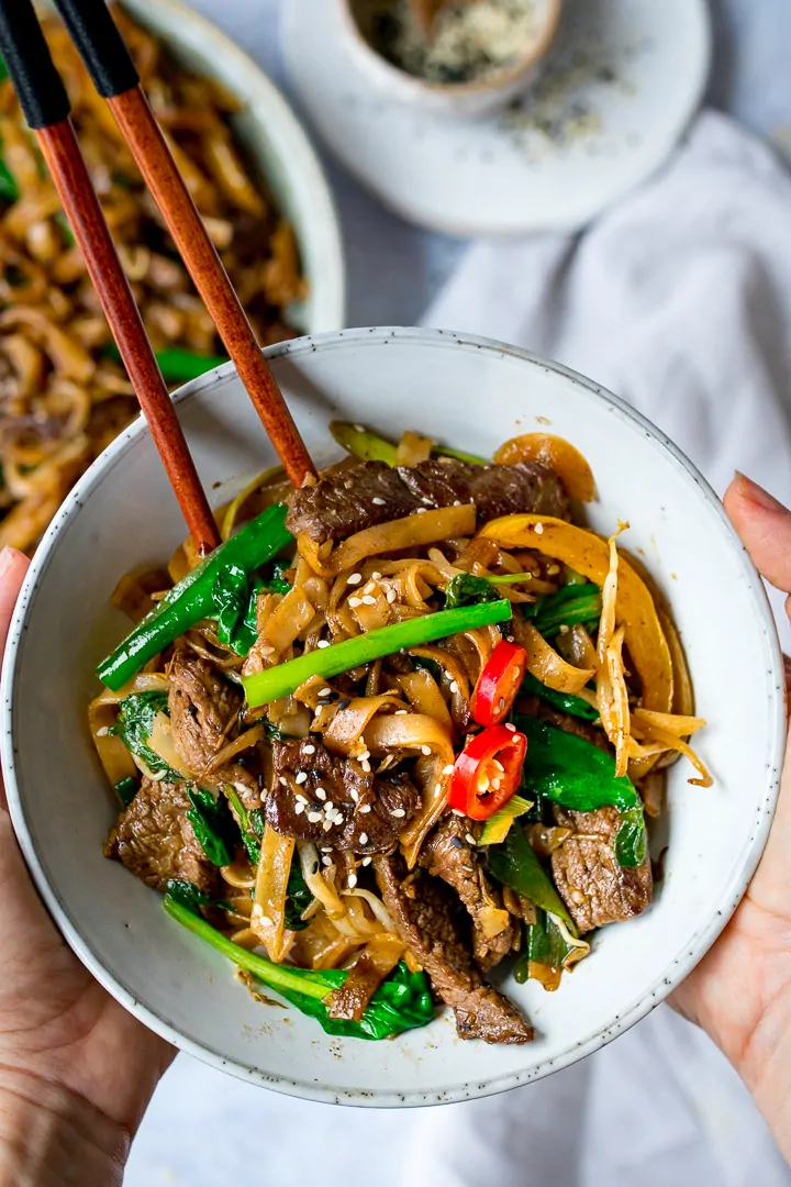 Hands holding bowl of Beef Chow Fun with chopsticks