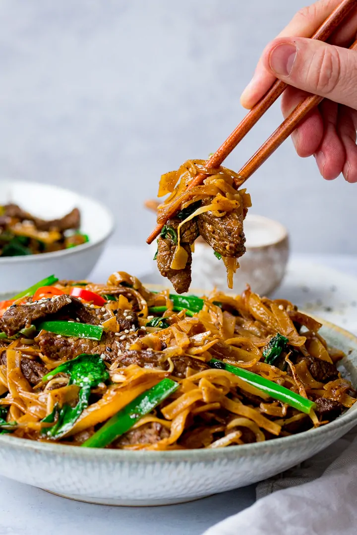 Beef Chow Fun being taken from a bowl with chopsticks