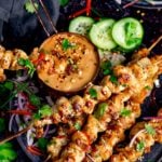 Square image of Chicken skewers with peanut satay sauce on a dark background