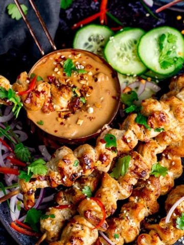 Square image of Chicken skewers with peanut satay sauce on a dark background