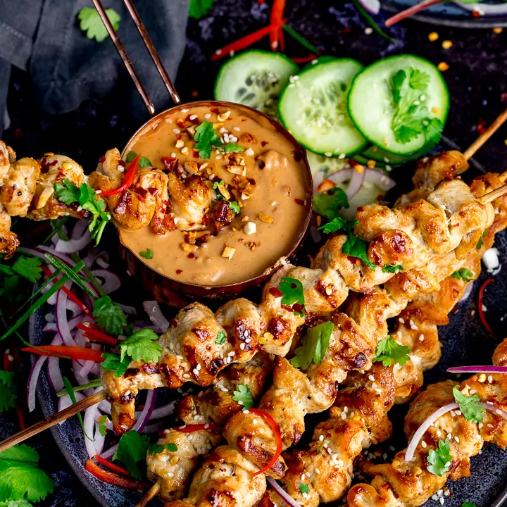 Square image of Chicken skewers with peanut satay sauce on a dark background