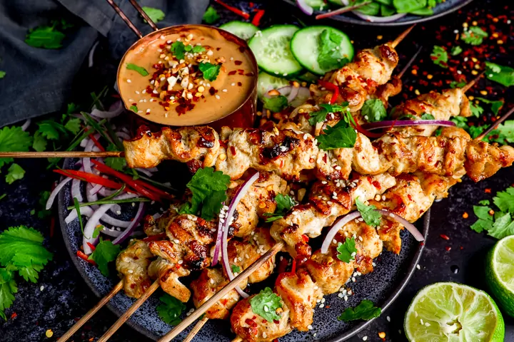 wide image of Chicken skewers with peanut satay sauce on a dark background