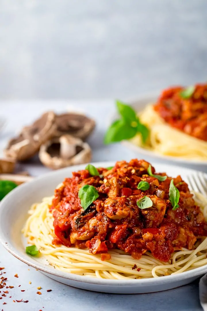 Plate of spaghetti topped with chicken and red pepper sauce on a light background