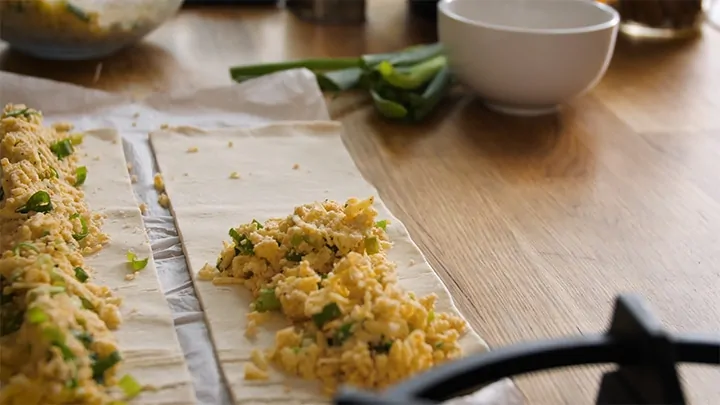 Cheese filling being spooned onto pastry for vegetarian sausage rolls