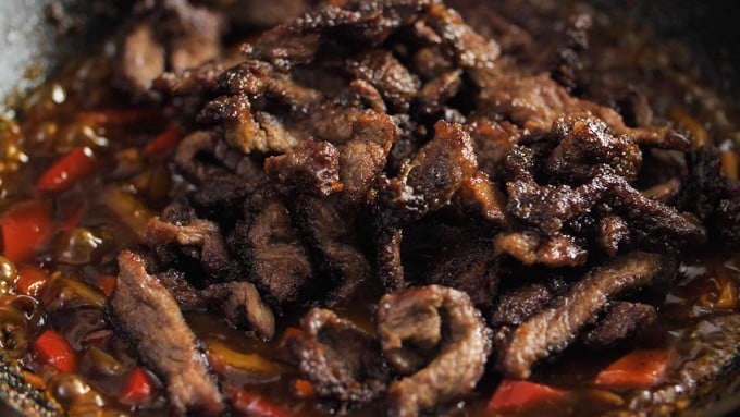 Fried beef strips in a wok with peppers and onions