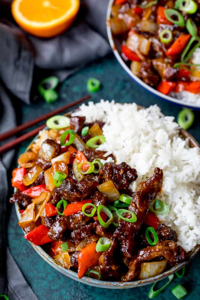 Two bowls of crispy orange beef with rice. Topped with spring onions.