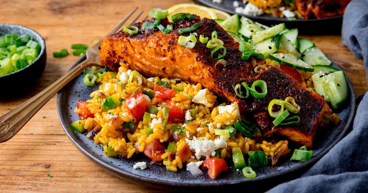 A crispy salmon fillet on top of vegetable rice with crumbled feta.