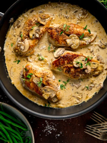 chicken in creamy white wine sauce in a dark pan next to a bowl of green beans