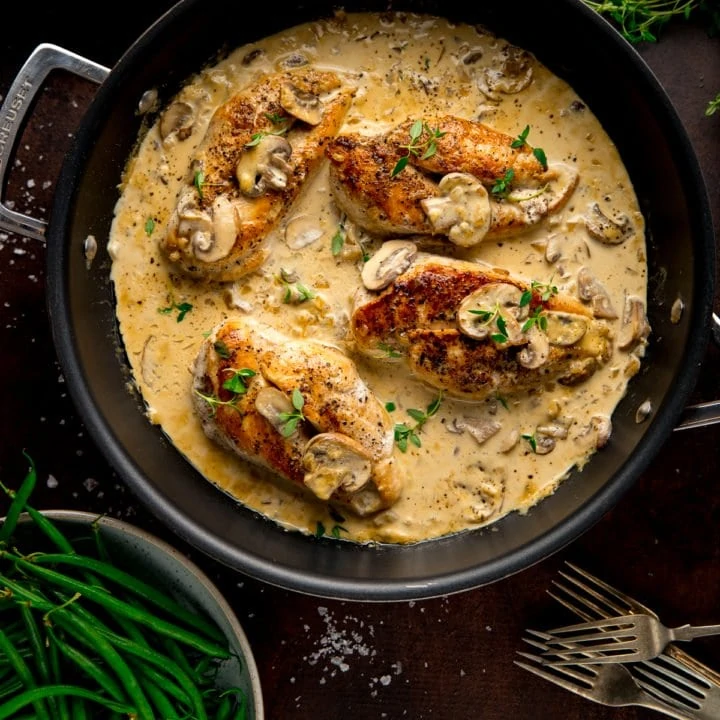 chicken in creamy white wine sauce in a dark pan next to a bowl of green beans