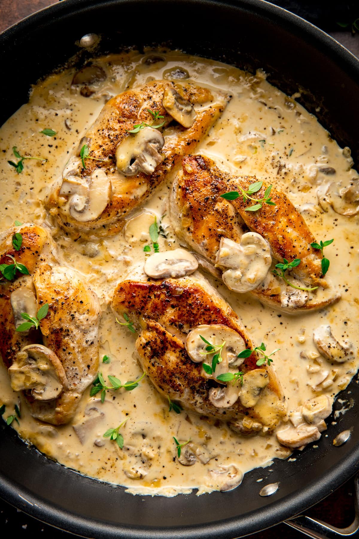 chicken in creamy white wine sauce with mushrooms in a black pan