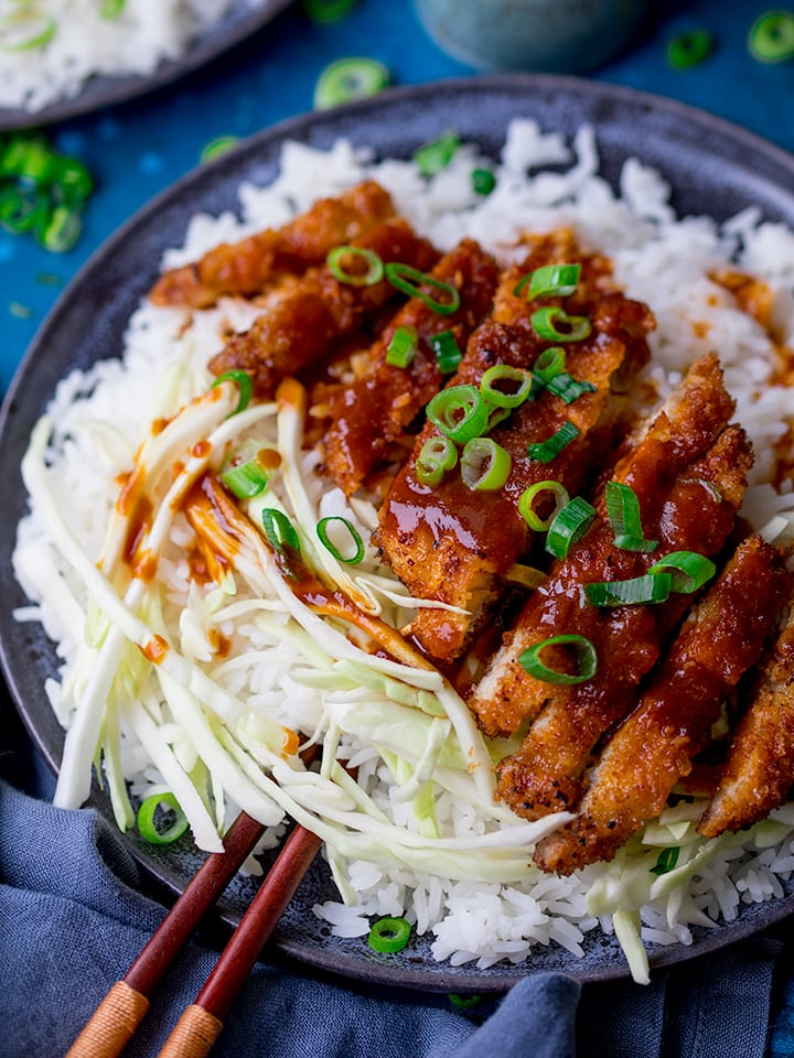 Tonkatsu pork curry on a plate with rice and cabbage. Spring onions sprinkled on top.