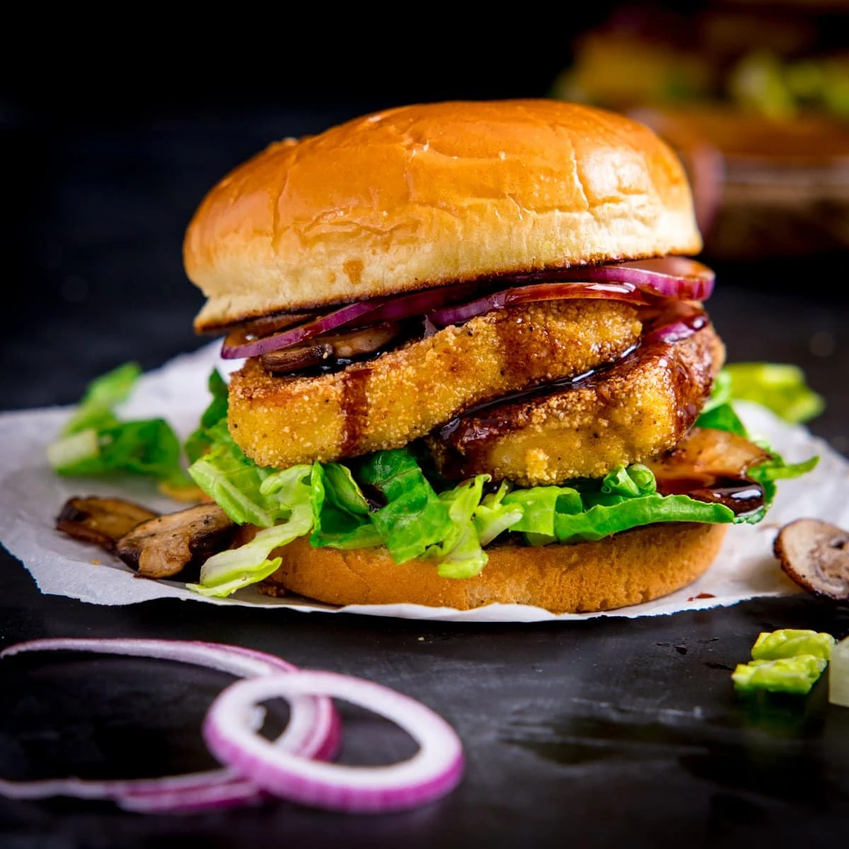 halloumi burger with lettuce and onions on a piece of parchment paper on a dark background