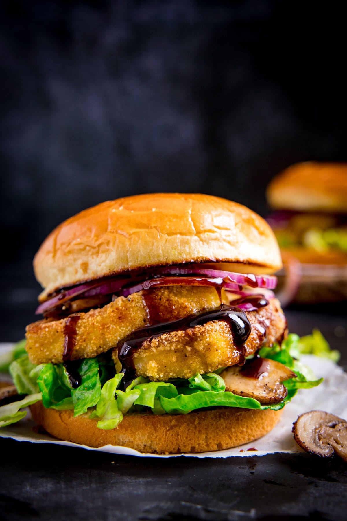 Side on image of a halloumi burger with lettuce sitting on a piece of parchment against a dark background