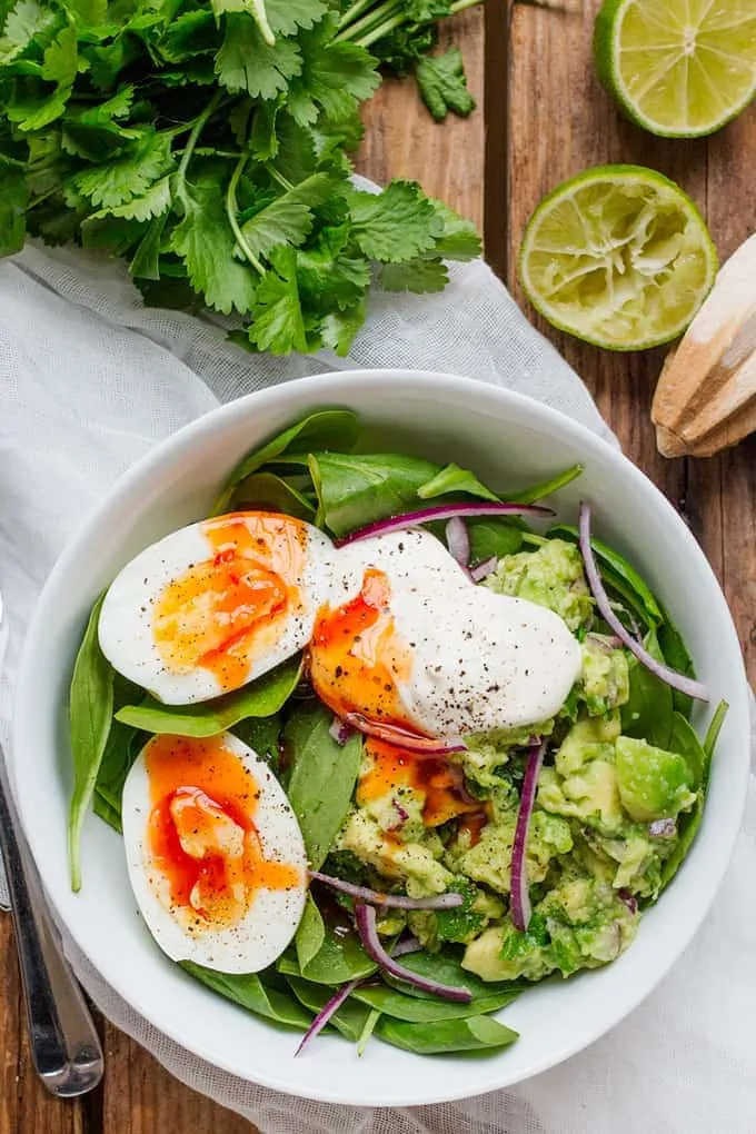 Overhead Photo of Guacamole and Egg Breakfast Bowl with Limes and Coriander in the background