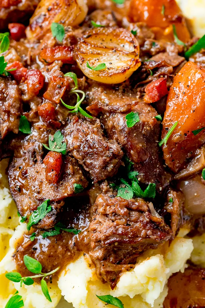 Close up of Beef Bourguignon on top of mashed potato, sprinkled with fresh thyme.