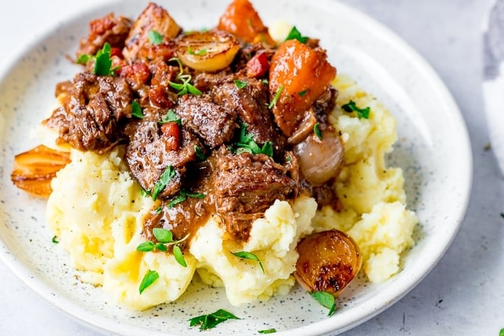 a plate of Beef Bourguignon on top of some mashed potato