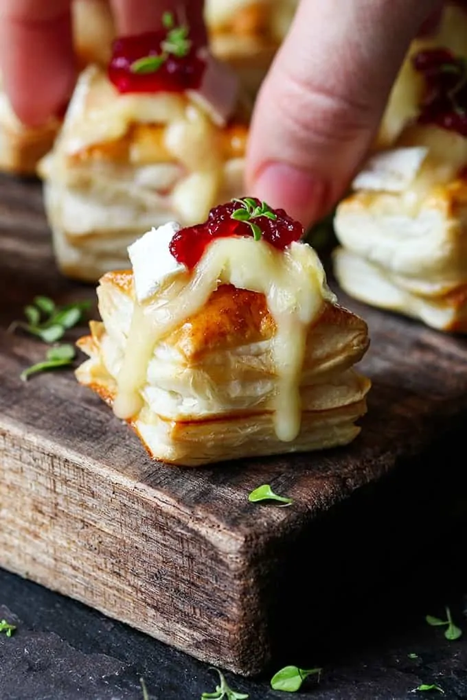 Cranberry and Brie bites on a wooden board with a hand taking one of the bites in the background