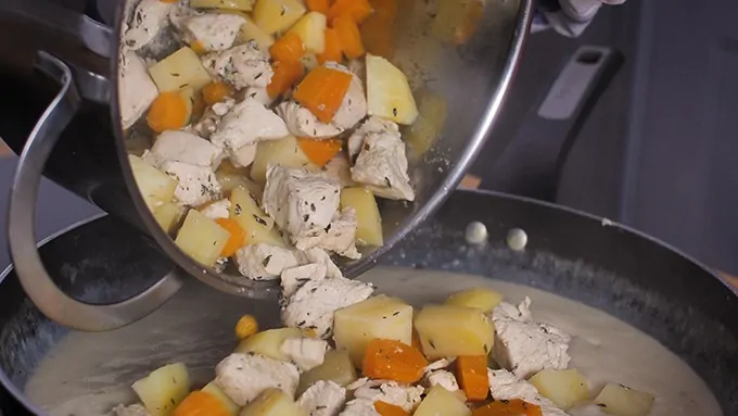 Adding chicken and vegetables to creamy sauce for pie filling