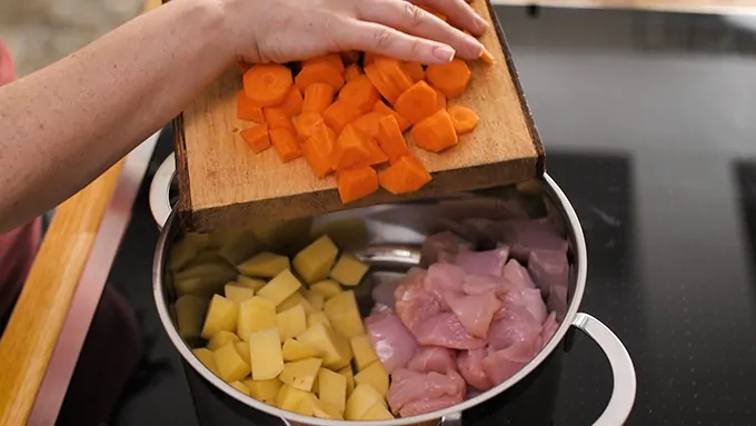 adding vegetables and chicken to pan for pie filling