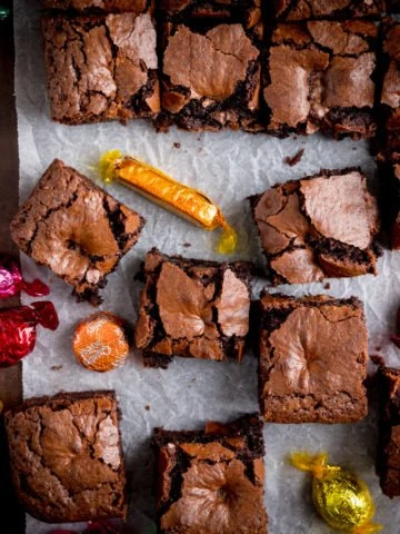 Overhead picture of some chocolate brownies on baking parchment with chocolates from the chocolate box scattered around.