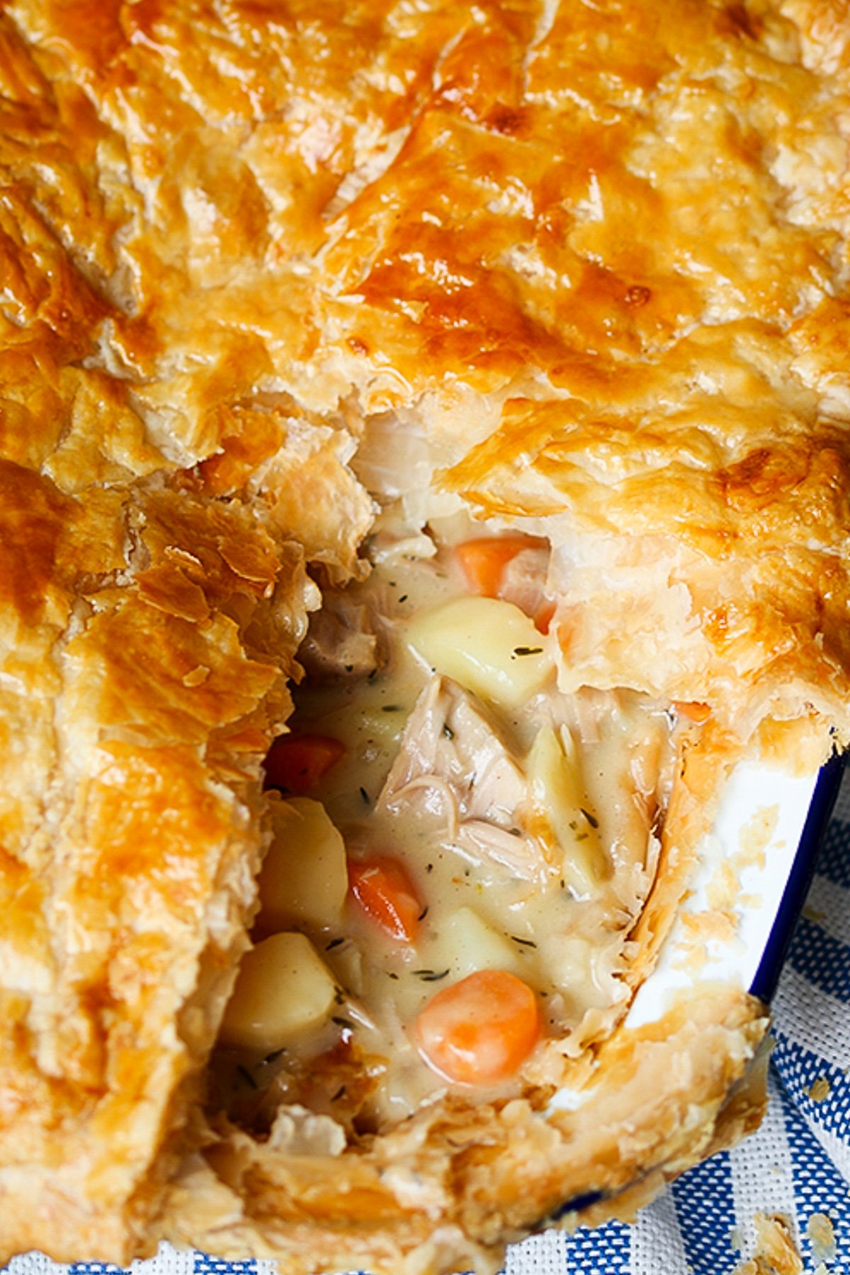 Side on angled close up photo Creamy Chicken and Vegetable puff pie with a slice taken out showing the carrots, chicken potato and creamy sauce inside