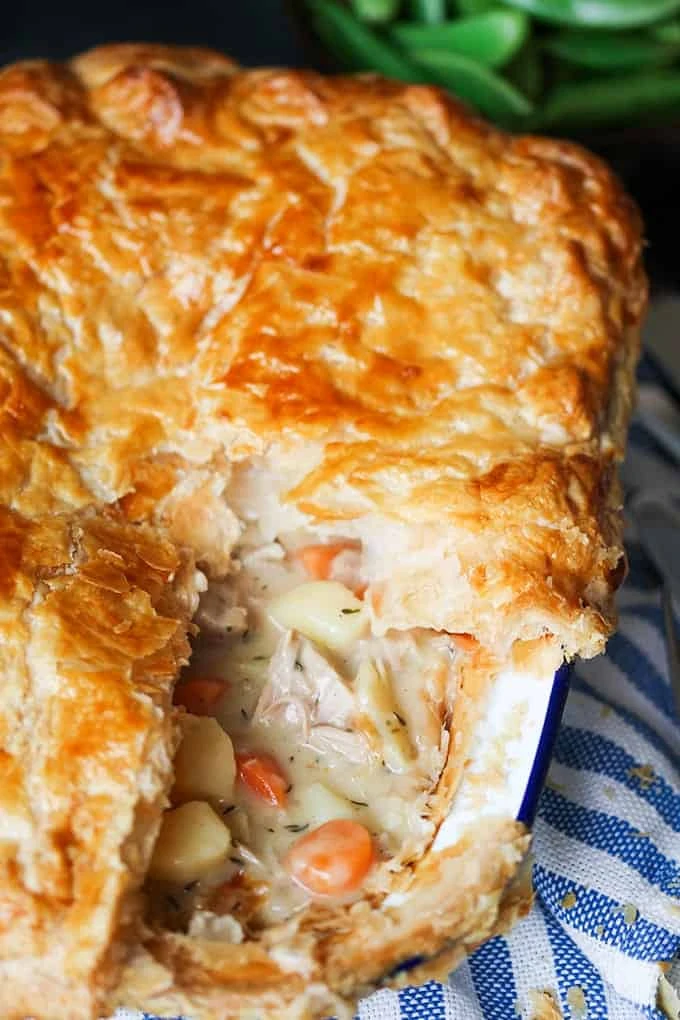 Side on angled close up photo Creamy Chicken and Vegetable puff pie with a slice taken out showing the carrots, chicken potato and creamy sauce inside