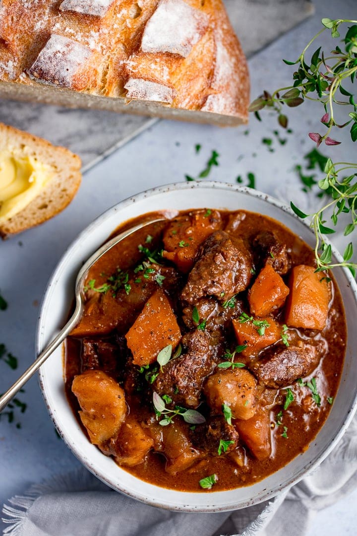 Bowl of Scottish beef stew with a spoon in it. Bread in the background.