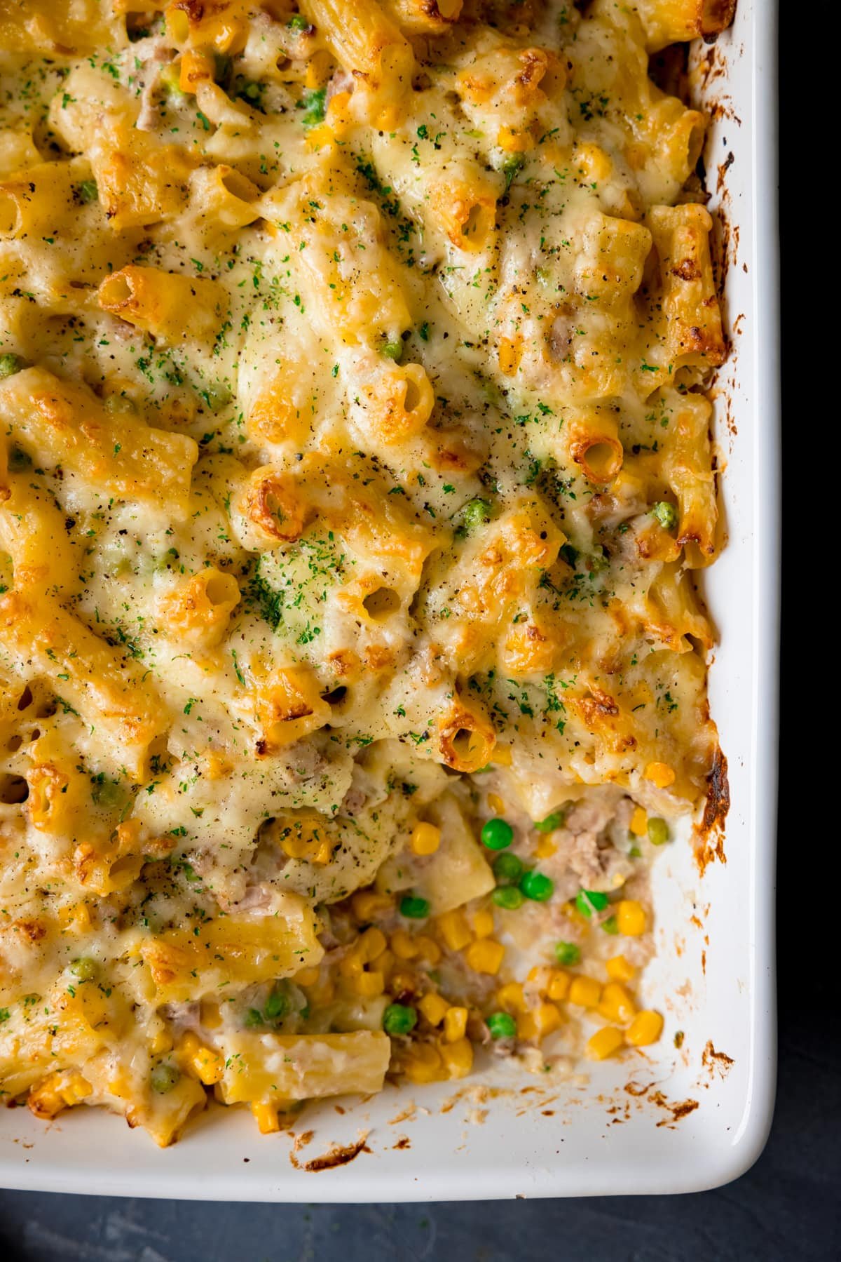 Overhead image of creamy tuna pasta bake in a white dish with a scoopful taken out.